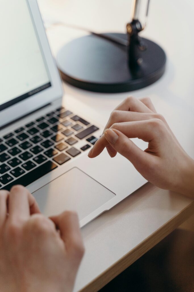 Close-up of hands using a laptop's touchpad in an office environment, highlighting focus and technology.